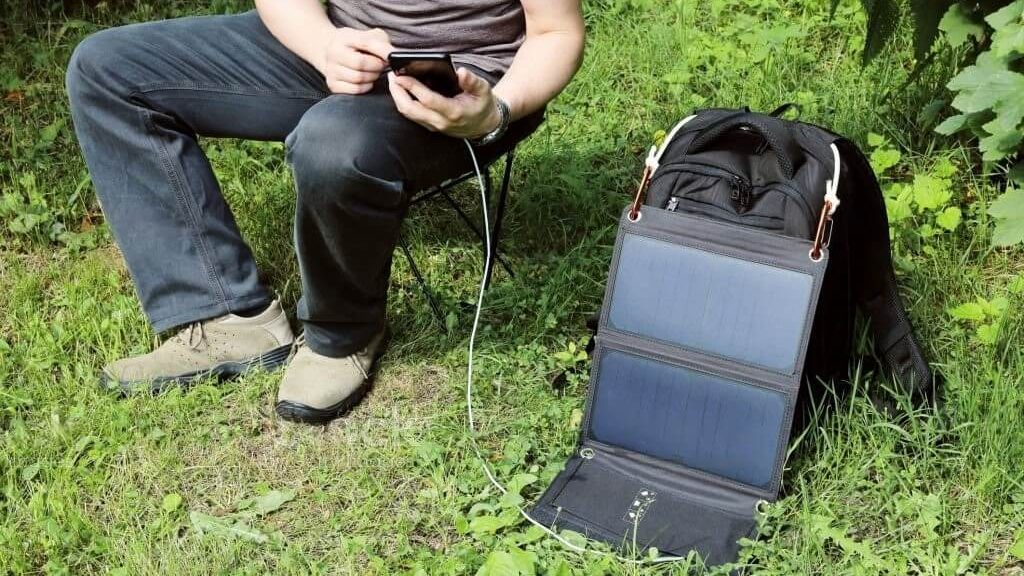 Una persona cargando su teléfono con un cargador solar, utilizando energía renovable para alimentar su dispositivo.